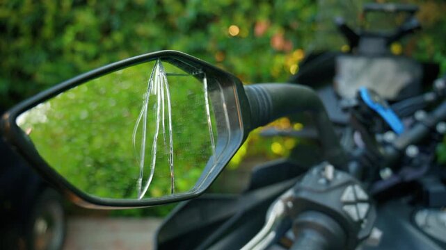 Motorcycle with a broken rearview mirror reflecting a blurred green background, emphasizing damage and the need for repair