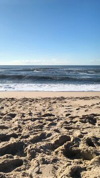 This serene, empty beach with heavily textured footprints in the sand and rolling blue ocean waves under a clear sky evokes peaceful solitude and coastal relaxation. Nobody is here.