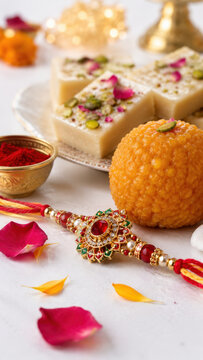 Jeweled rakhi beside laddu barfi festive sweets platter, raksha bandhan festival, rakhi bracelet with indian sweets, traditional sibling celebration, family ritual, indian cultural holiday