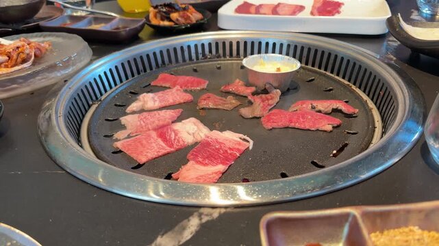 Raw meat slices and chicken, beef and squid pieces cooking tabletop built in asian barbecue grill restaurant, grilling on hot metal plate, BBQ cooking process, Group friends enjoying delicious food