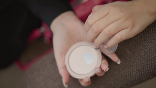 Overhead view shows hands holding open round makeup compact as fingertip samples cosmetic powder on textured surface, capturing gentle touch, subtle motion, and relaxed beauty routine indoors