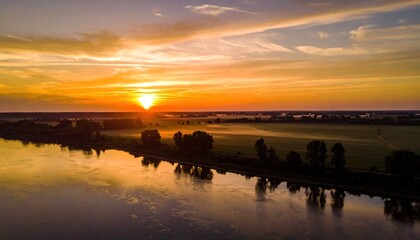 Naklejka premium Aerial view of river at sunrise, golden sun illuminating landscape with trees and mist