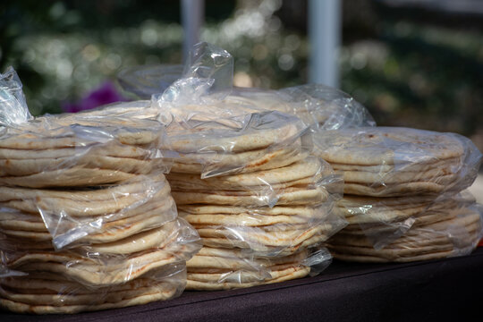 Clear plastic bags filled with baked whole wheat Greek pita breads. The gluten free flour based round wraps are homemade and sold at a market. The Mexican food packages are stacked on a table for sale