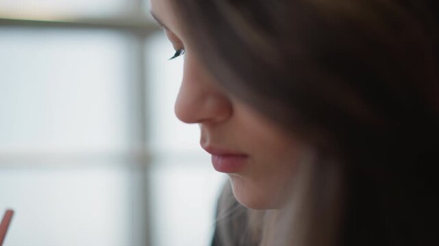 Intimate close side profile of young woman looking downward beside soft window light, relaxed lips and lowered eyelids creating calm contemplative mood with focused indoor feeling, with woman