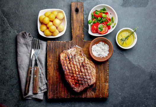 Grilled beef steak served on wooden table with tomato salad and potatoes balls. Barbecue, bbq meat beef tenderloin. Top view, slate background