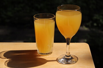 Glasses of orange juice on a wood table in the garden with a space for writing. Fruit juice in summer with a green background and vegetation. Refreshment and natural juice in orange color. © Martine