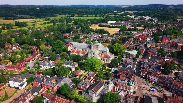 Drone shot showing Romsey Abbey nestled among trees and rooftops, with open Hampshire countryside behind.