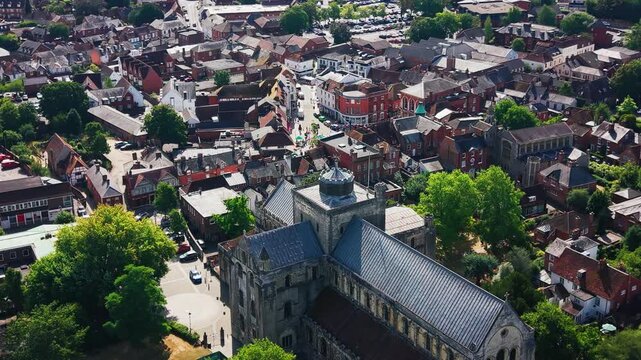 Drone shot low over Romsey Abbey's tower and nave, with the town's high street and shops beyond.