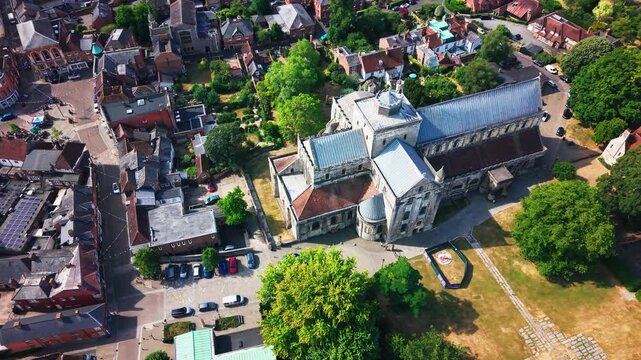 Drone shot close over Romsey Abbey's long nave roof, tower and rounded apse end, town beyond.
