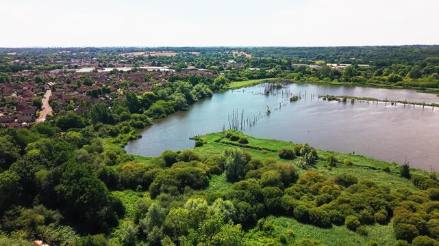 Drone shot over Fishlake Meadows' flooded wetland lake, bordered by dead trees and Romsey rooftops beyond.