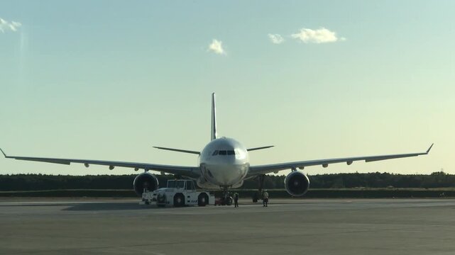 Commercial passenger airplane being pulled by a tow tractor on the airport tarmac with ground crew walking alongside