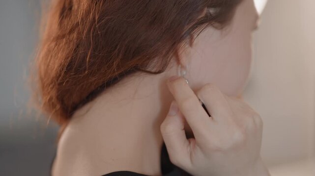 Rear close-up of person securing stud earring at earlobe, fingers guiding post into metal clasp with gentle precision, slight head tilt and calm focused mood, soft indoor light highlighting skin