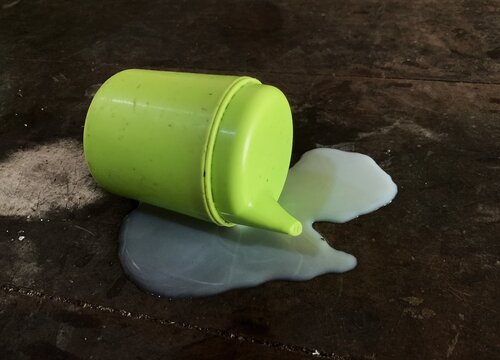 Overturned green sippy cup with spilled milk on wooden surface. weathered wood.
