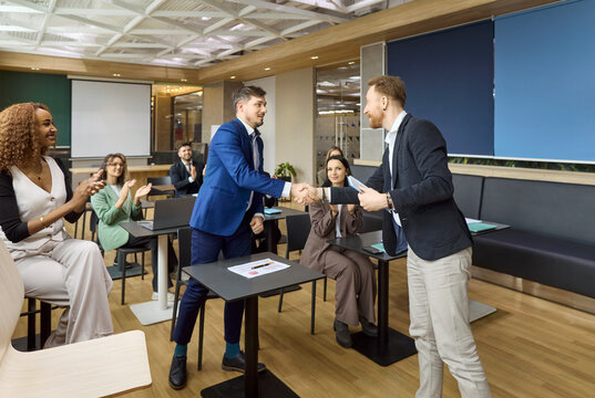 Businessmen handshake confirms agreement at team meeting. Colleagues give applause in an office as a contract is signed, marking success and partnership. Clear concept of partnership success.