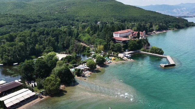 Aerial drone view of St Naum Monastery and Black Drin Springs near Lake Ohrid, North Macedonia, with clear water, boats, lush greenery and sunny summer landscape