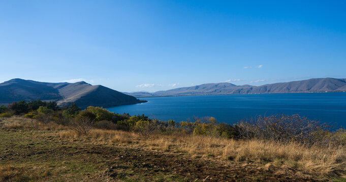 View of Lake Sevan surrounded by rolling mountains and autumn grassland under a bright clear blue sky, Armenia.