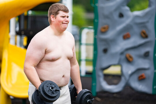 Workout begins on playground. Overweight workout shows effort. Outdoor workout with dumbbells. Workout supports healthy lifestyle.