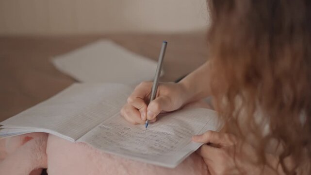 Over--shoulder close-up of person writing in open notebook on lap; visible action shows pen making notes and slight page movement indicating ongoing writing while head tilts toward page in focused
