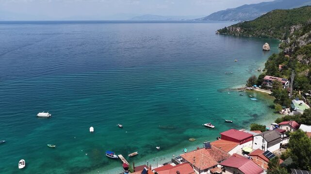 Aerial drone view of Trpejca village on Lake Ohrid, North Macedonia, traditional buildings, crystal clear turquoise lake water, rocky shoreline and beautiful lakeside beach