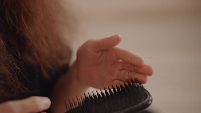 Tight close-up of hand brushing long hair with paddle brush, visible downward motion as bristles separate strands and fingers glide over brush