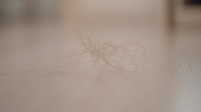 Low-angle close-up showing small clump of dust, lint, and hair resting and slightly drifting across neutral matte indoor floor