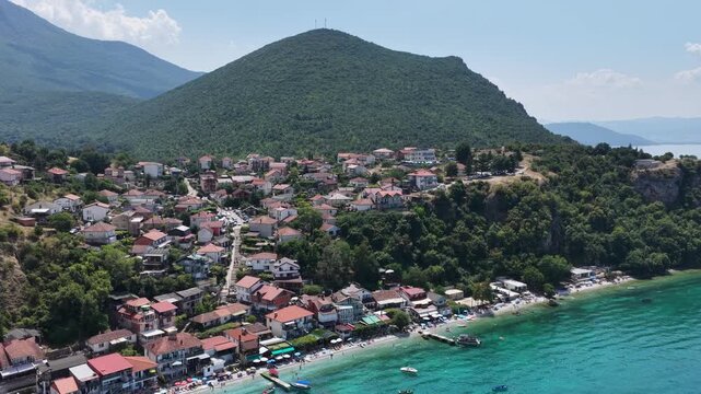 Aerial drone view of Trpejca village on Lake Ohrid, North Macedonia, traditional buildings, crystal clear turquoise lake water, rocky shoreline and beautiful lakeside beach