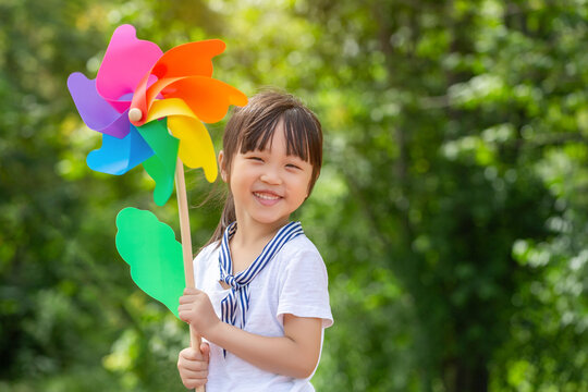 Portrait of a happy smiling girl holding a colorful pinwheel against a blurry green foliage background.