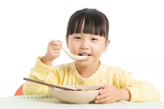 Happy Asian Little Girl Eating Porridge with Spoon at Dining Table Isolated on White Background