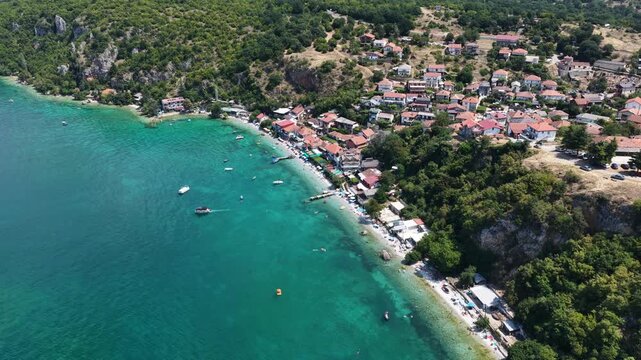 Aerial drone view of Trpejca village on Lake Ohrid, North Macedonia, traditional buildings, crystal clear turquoise lake water, rocky shoreline and beautiful lakeside beach
