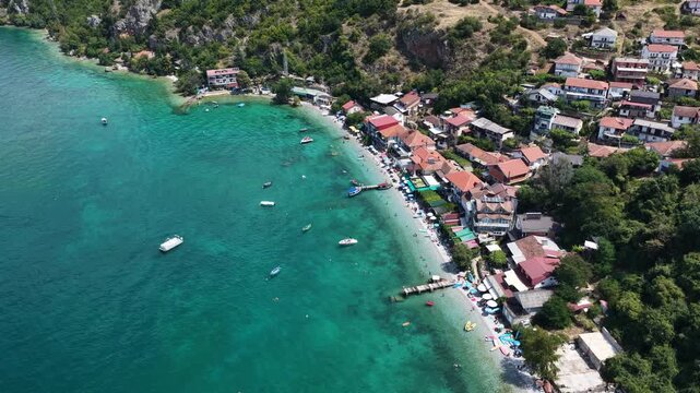 Aerial drone view of Trpejca village on Lake Ohrid, North Macedonia, traditional buildings, crystal clear turquoise lake water, rocky shoreline and beautiful lakeside beach