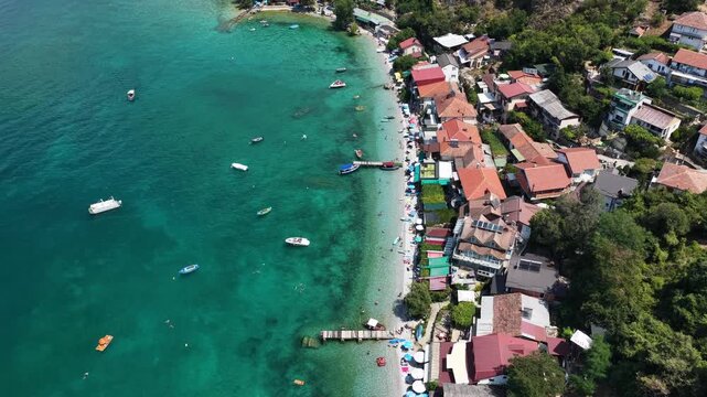 Aerial drone view of Trpejca village on Lake Ohrid, North Macedonia, traditional buildings, crystal clear turquoise lake water, rocky shoreline and beautiful lakeside beach