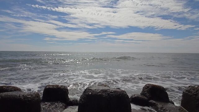 Ocean waves crashing near concrete wave breakers under a blue sky