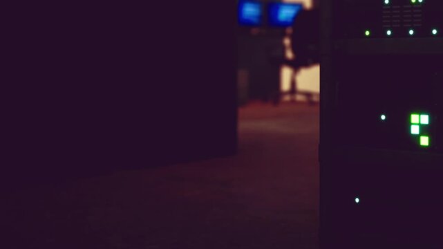 A server room shows rows of servers with blinking lights. The area is dark with some light from screens in the background. It looks busy and focused on technology work.
