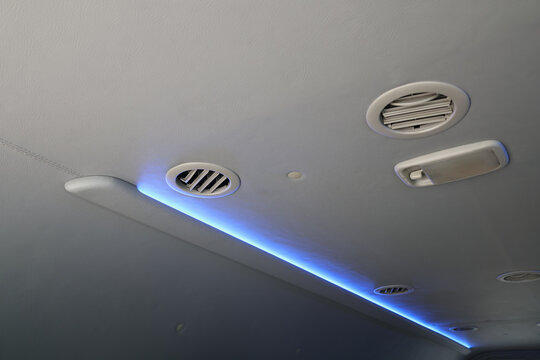 Blue light strip illuminates vehicle ceiling with air vent, overhead handle, and interior roof panel, creating modern atmosphere inside passenger transport