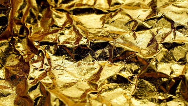 Shiny gold foil texture featuring deep crinkles and reflective metallic surfaces captured in bright natural light