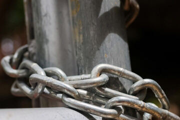 Naklejka premium Metal chain wrapped around weathered post, showing security, restraint, and industrial texture in close up detail