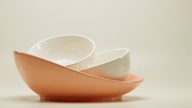 Minimalist ceramic bowls in pastel orange and cream stacked elegantly on a soft neutral studio background