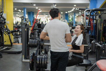 Fototapeta premium Asian man and woman taking rest break chatting and wiping sweat in gym