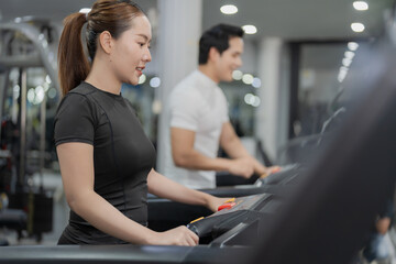 Fototapeta premium Asian man pressing touchscreen display on treadmill with personal trainer or gym partner in background