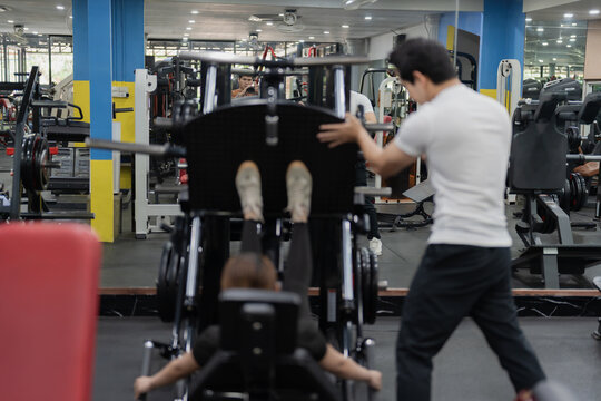 Asian woman working out on chest press machine with male personal trainer assistance in gym