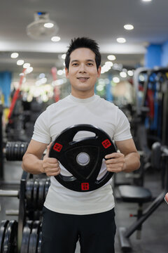 Asian man sitting on workout bench doing bicep curls with dumbbells in gym