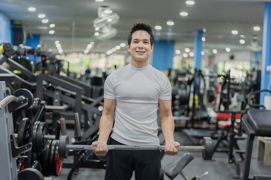 Asian man sitting on workout bench doing bicep curls with dumbbells in gym