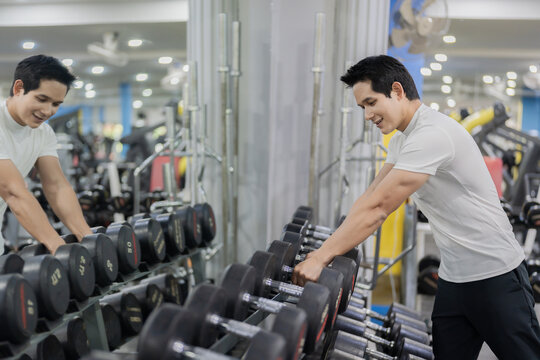 Asian man sitting on workout bench doing bicep curls with dumbbells in gym