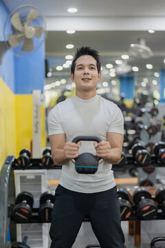 Asian man sitting on workout bench doing bicep curls with dumbbells in gym