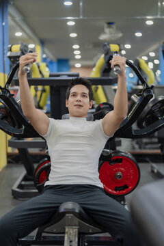Asian man lifting barbell on bench press with female personal trainer supervising in gym