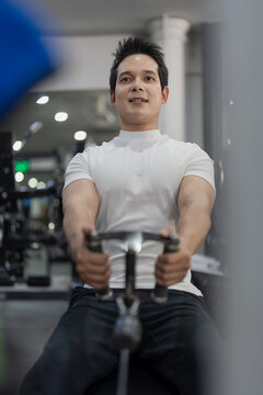 Asian man performing seated cable row exercise on machine in gym