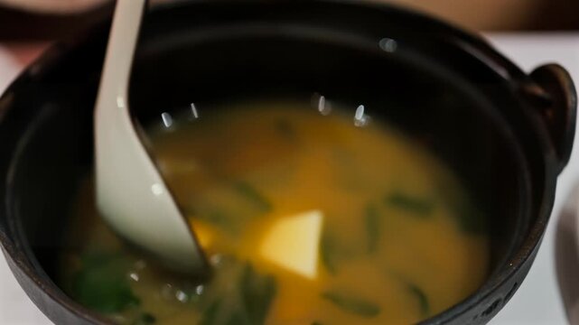 Close up shot of japanese miso soup with tofu and greens being served with a spoon.