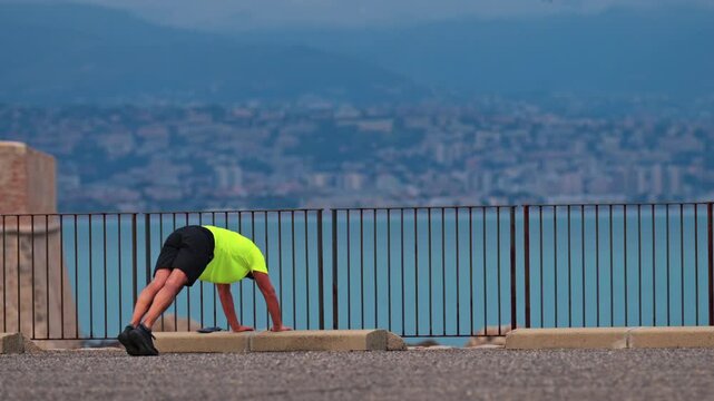 Man performing pike pushups outdoors during morning workout near ocean.