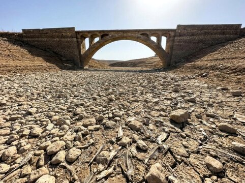 Historical stone arch bridge spanning a completely dried riverbed with cracked mud