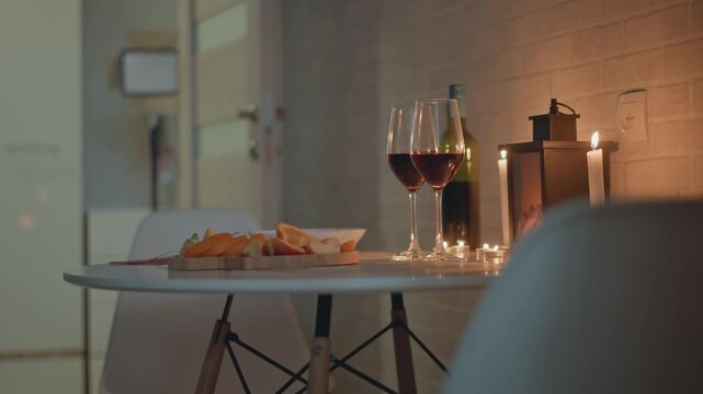Low-angle interior view of intimate evening table setup with red wine glasses, bread bowl, coffee press, and lit candle, casting warm glow, soft reflections, and relaxed hospitality mood